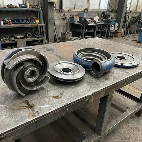 slurry-pump-wet-end-wear-parts-layout Separate slurry pump wet-end showing high-chrome impeller, throatbush, volute liner, and frame plate liner on a clean workbench for identifying and stocking sacrificial slurry pump wear parts.